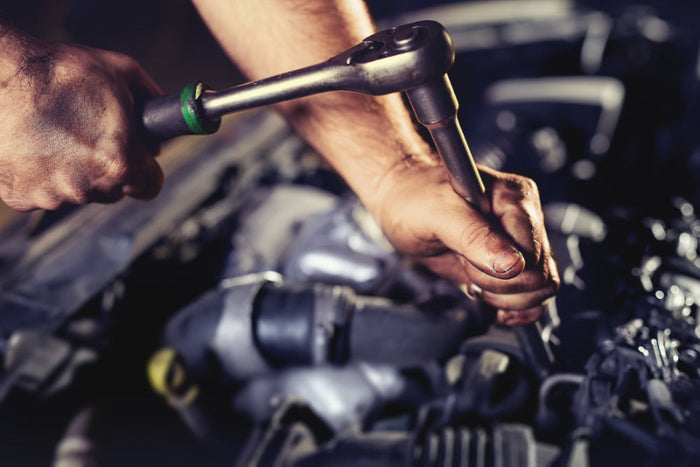 Close-up of hands using a wrench on a mechanical engine.