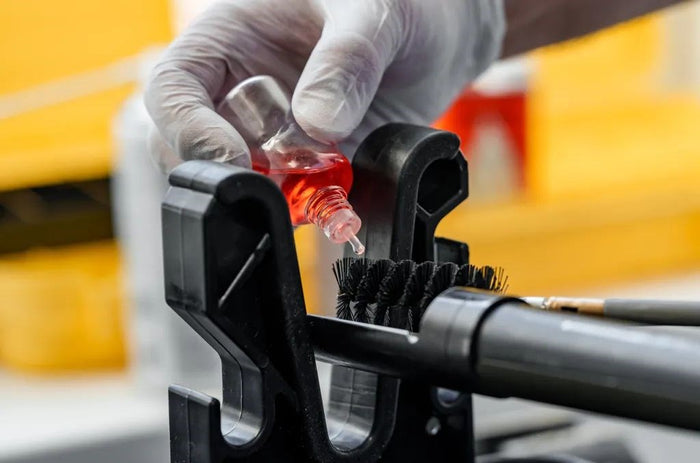 Person applying red liquid to a black brush attached to a cleaning tool with a blurred background